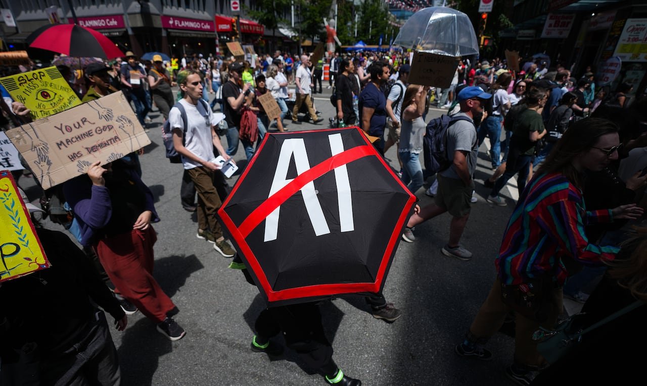 default-107 A large group of people are outside protesting. At the centre is an umbrella that has "AI" with a big slash over it.
